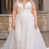 Woman wearing an ivory chiffon wedding dress standing outdoors.

Sydney's Closet style SC5360 in ivory/nude. Plus size light flowy chiffon bridal dress with pleated bodice and pleated waistband.  Illusion back covered in lace appliques with crystal buttons. Available in sizes 14-40. 
