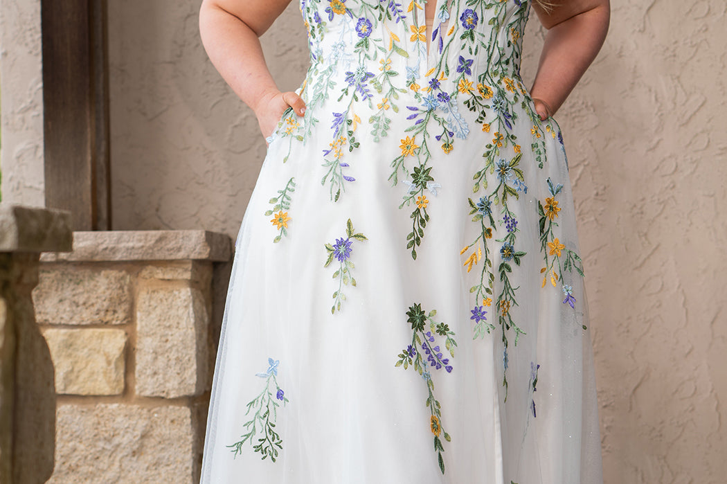 Sydney's Closet SC5371 plus size wedding dress.  Multi-colored floral lace on ivory tulle. Sexy plunging V-neckline with exposed corset boning.  Basque waistline on A-line skirt with slit and long train with lace details. Perfect for the unique, trendy bride.