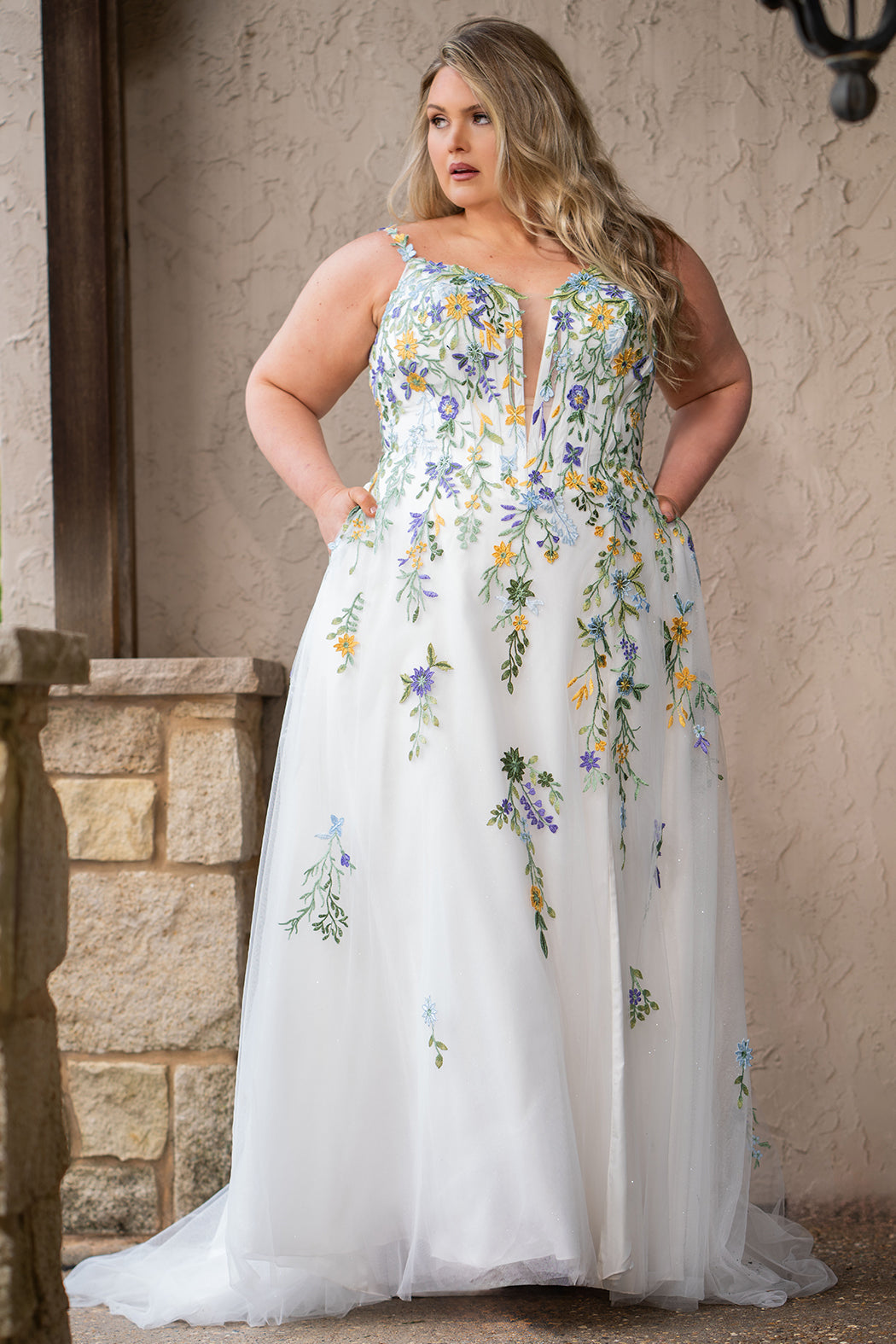 Sydney's Closet SC5371 plus size wedding dress.  Multi-colored floral lace on ivory tulle. Sexy plunging V-neckline with exposed corset boning.  Basque waistline on A-line skirt with slit and long train with lace details. Perfect for the unique, trendy bride.