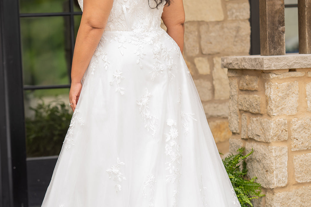 Sydney's Closet SC5372 plus size wedding dress.  Ivory floral lace on ivory tulle. Sexy plunging V-neckline with exposed corset boning.  Basque waistline on A-line skirt with slit and long train with lace details. 