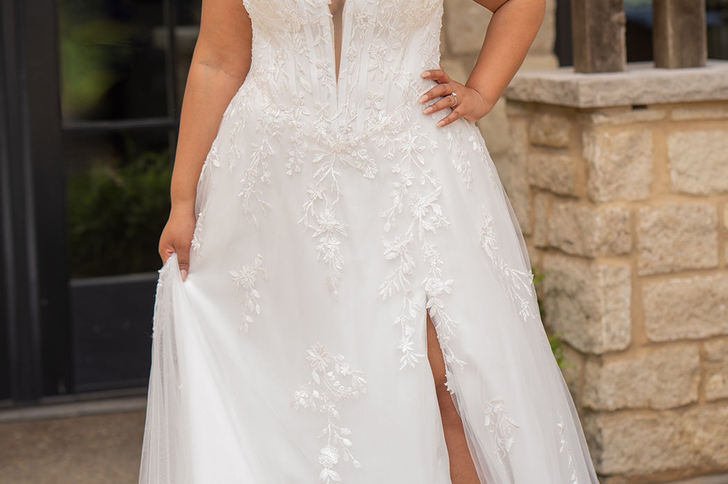 Sydney's Closet SC5372 plus size wedding dress.  Ivory floral lace on ivory tulle. Sexy plunging V-neckline with exposed corset boning.  Basque waistline on A-line skirt with slit and long train with lace details. 