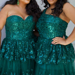 SC7398 & SC7399 duo picture outside for prom 2025. 

Strapless, sweetheart plus size gala formal ballgown. Exposed corset boning on bodice covered in lace applqiues. Tiered A-line skirt with matching lace applique hem. Style SC7398 is available in forest green, navy blue or burgundy red by Sydney's Closet. 

Plus size one-shoulder formal gala Mardi Gras gown with embroidered sequin lace appliques on bodice and on tiered A-line skirt with slit. Available in forest green. navy blue and burgundy r
