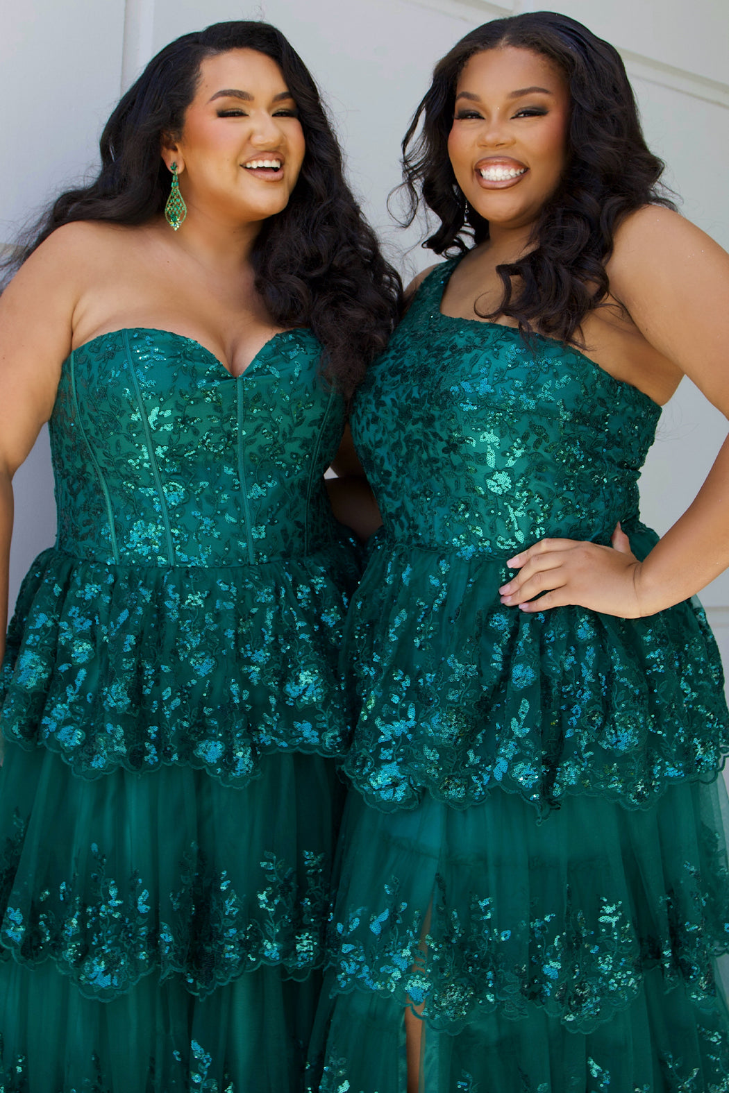 SC7398 & SC7399 duo picture outside for prom 2025. 

Strapless, sweetheart plus size gala formal ballgown. Exposed corset boning on bodice covered in lace applqiues. Tiered A-line skirt with matching lace applique hem. Style SC7398 is available in forest green, navy blue or burgundy red by Sydney's Closet. 

Plus size one-shoulder formal gala Mardi Gras gown with embroidered sequin lace appliques on bodice and on tiered A-line skirt with slit. Available in forest green. navy blue and burgundy r
