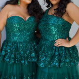 SC7398 & SC7399 duo picture outside for prom 2025. 

Strapless, sweetheart plus size gala formal ballgown. Exposed corset boning on bodice covered in lace applqiues. Tiered A-line skirt with matching lace applique hem. Style SC7398 is available in forest green, navy blue or burgundy red by Sydney's Closet. 

Plus size one-shoulder formal gala Mardi Gras gown with embroidered sequin lace appliques on bodice and on tiered A-line skirt with slit. Available in forest green. navy blue and burgundy r