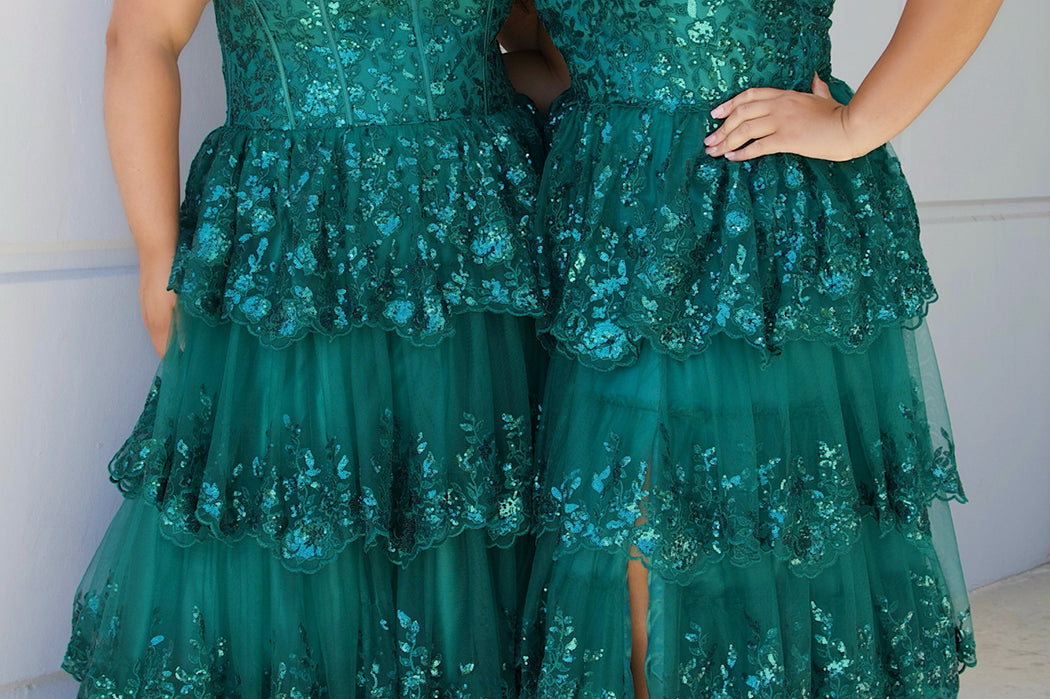 SC7398 & SC7399 duo picture outside for prom 2025. 

Strapless, sweetheart plus size gala formal ballgown. Exposed corset boning on bodice covered in lace applqiues. Tiered A-line skirt with matching lace applique hem. Style SC7398 is available in forest green, navy blue or burgundy red by Sydney's Closet. 

Plus size one-shoulder formal gala Mardi Gras gown with embroidered sequin lace appliques on bodice and on tiered A-line skirt with slit. Available in forest green. navy blue and burgundy r