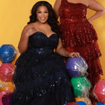 SC7398 & SC7399 duo picture with oversized candy for prom 2025. 

Strapless, sweetheart plus size gala formal ballgown. Exposed corset boning on bodice covered in lace applqiues. Tiered A-line skirt with matching lace applique hem. Style SC7398 is available in forest green, navy blue or burgundy red by Sydney's Closet. 

Plus size one-shoulder formal gala Mardi Gras gown with embroidered sequin lace appliques on bodice and on tiered A-line skirt with slit. Available in forest green. navy blue and burgundy r