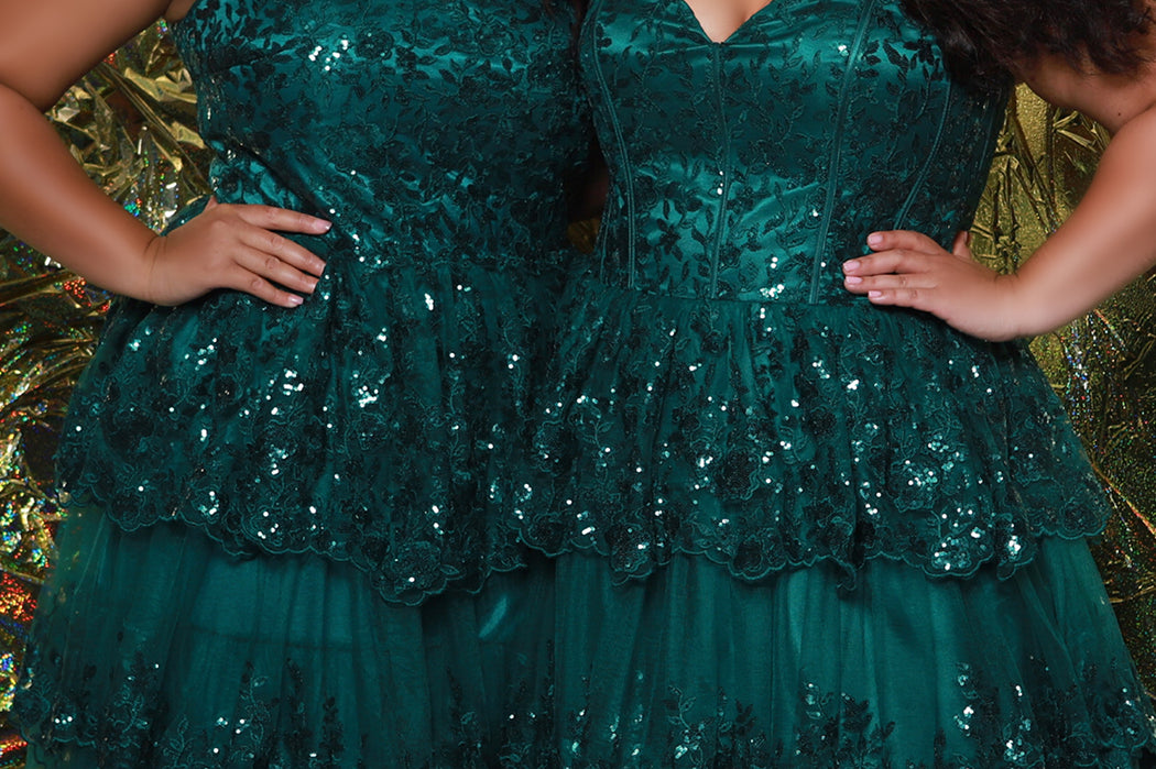 SC7398 & SC7399 duo picture with oversized candy for prom 2025. 

Strapless, sweetheart plus size gala formal ballgown. Exposed corset boning on bodice covered in lace applqiues. Tiered A-line skirt with matching lace applique hem. Style SC7398 is available in forest green, navy blue or burgundy red by Sydney's Closet. 

Plus size one-shoulder formal gala Mardi Gras gown with embroidered sequin lace appliques on bodice and on tiered A-line skirt with slit. Available in forest green. navy blue and burgundy r