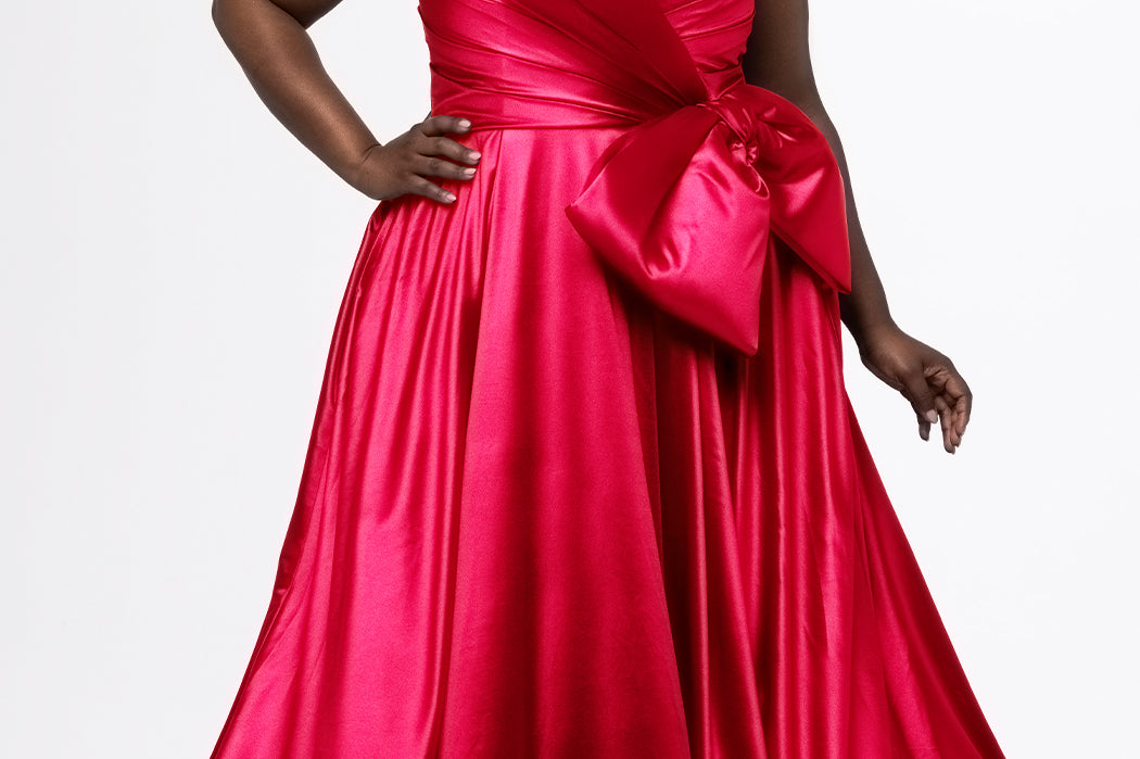 Sydney's Closet style SC7437 in pink. 

Plus size A-line formal dress with strapless, pleated bodice, natural waistline with detachable oversized bow, A-line skirt with horsehair hem in silky satin fabric.