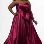 Sydney's Closet style SC7437 in wine. 

Plus size A-line formal dress with strapless, pleated bodice, natural waistline with detachable oversized bow, A-line skirt with horsehair hem in silky satin fabric.