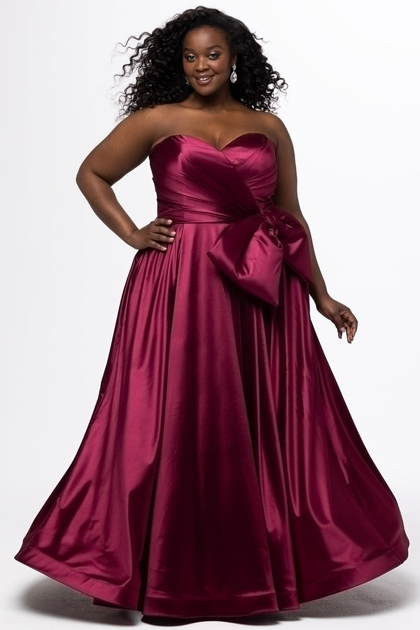 Sydney's Closet style SC7437 in wine. 

Plus size A-line formal dress with strapless, pleated bodice, natural waistline with detachable oversized bow, A-line skirt with horsehair hem in silky satin fabric.