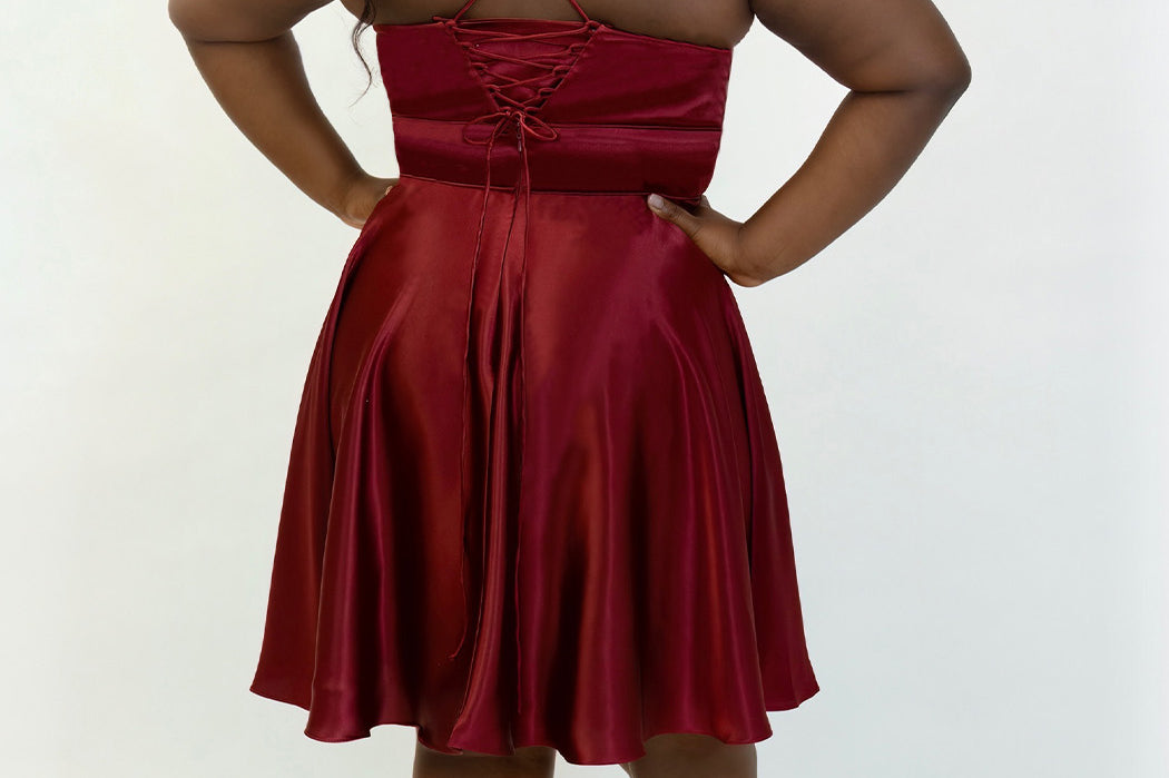 This is SC8124 in our Sydney's Closet Homecoming collection. This plus size party dress comes in black, red, green, and blue! This dress has spaghetti straps that turn into a corset back! This a-line satin gown flows beautifully with your dance moves! With the length hitting right at your knees, and pockets, it is the perfect dress for this homecoming season!