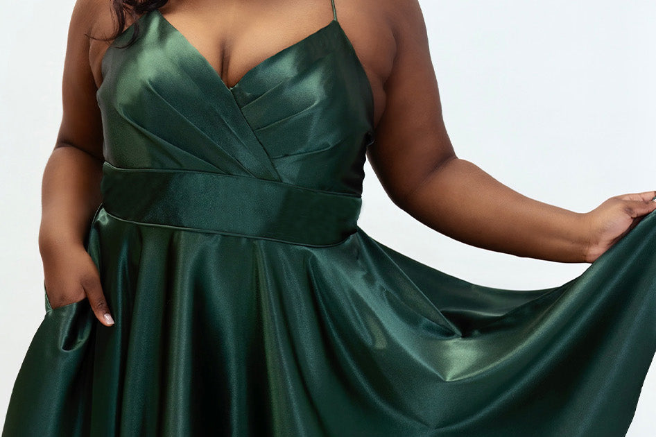 This is SC8124 in our Sydney's Closet Homecoming collection. This plus size party dress comes in black, red, green, and blue! This dress has spaghetti straps, a v neckline, and a beautiful rouched bodice! This a-line satin gown flows beautifully with your dance moves! With the length hitting right at your knees, and pockets, it is the perfect dress for this homecoming season!