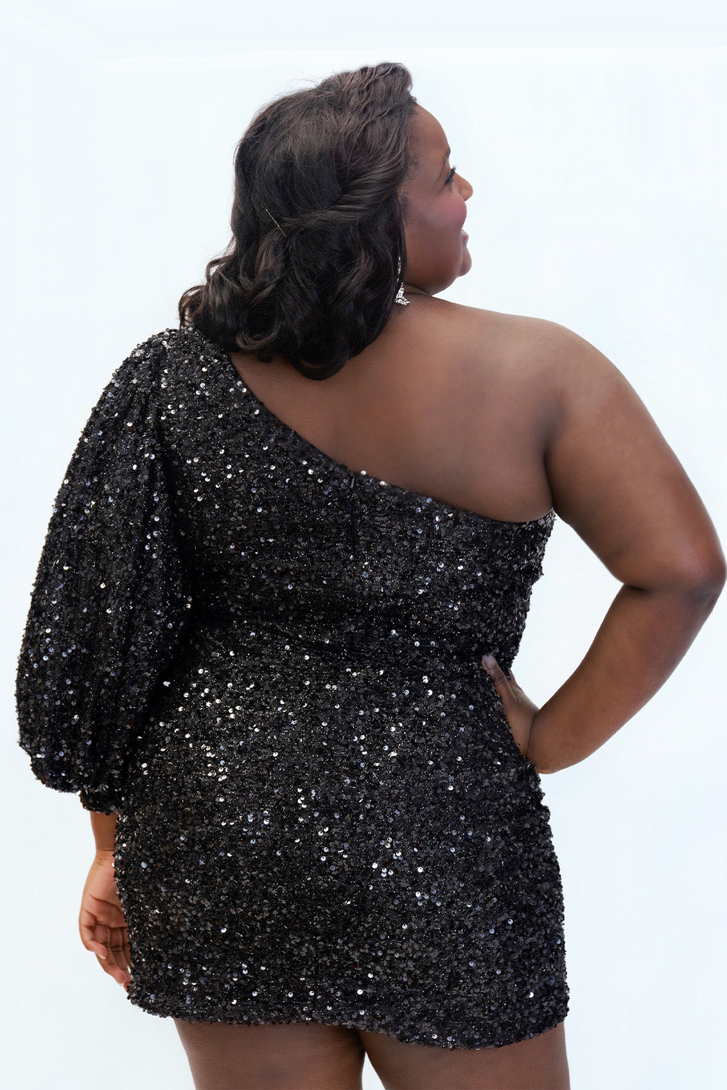 This is SC8133 in our Sydney's Closet Homecoming collection. This plus size party dress comes in black, blue, purple, and red! This dress has a one shoulder long sleeve pouf sleeve, a cutout bodice, and a natural waistline. This fitted all over sequin dress has the spotlight as the most perfect dress for this homecoming season!