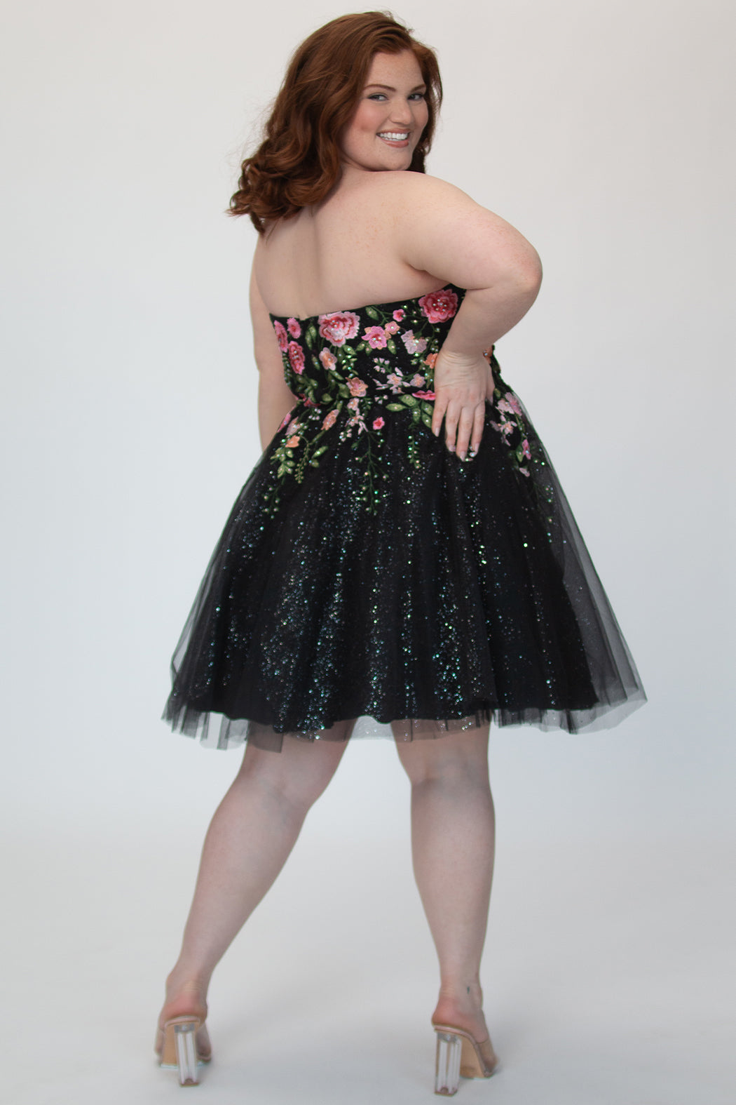 SC8137 Back view. Black sparkle tulle short a-line party dress with pink floral embroidered roses. Strapless sweetheart neckline, long invisible center back zipper.  Available only in black floral. Curvy sizes 10-32. Model in picture is 5 foot 9 inches and a size 16.