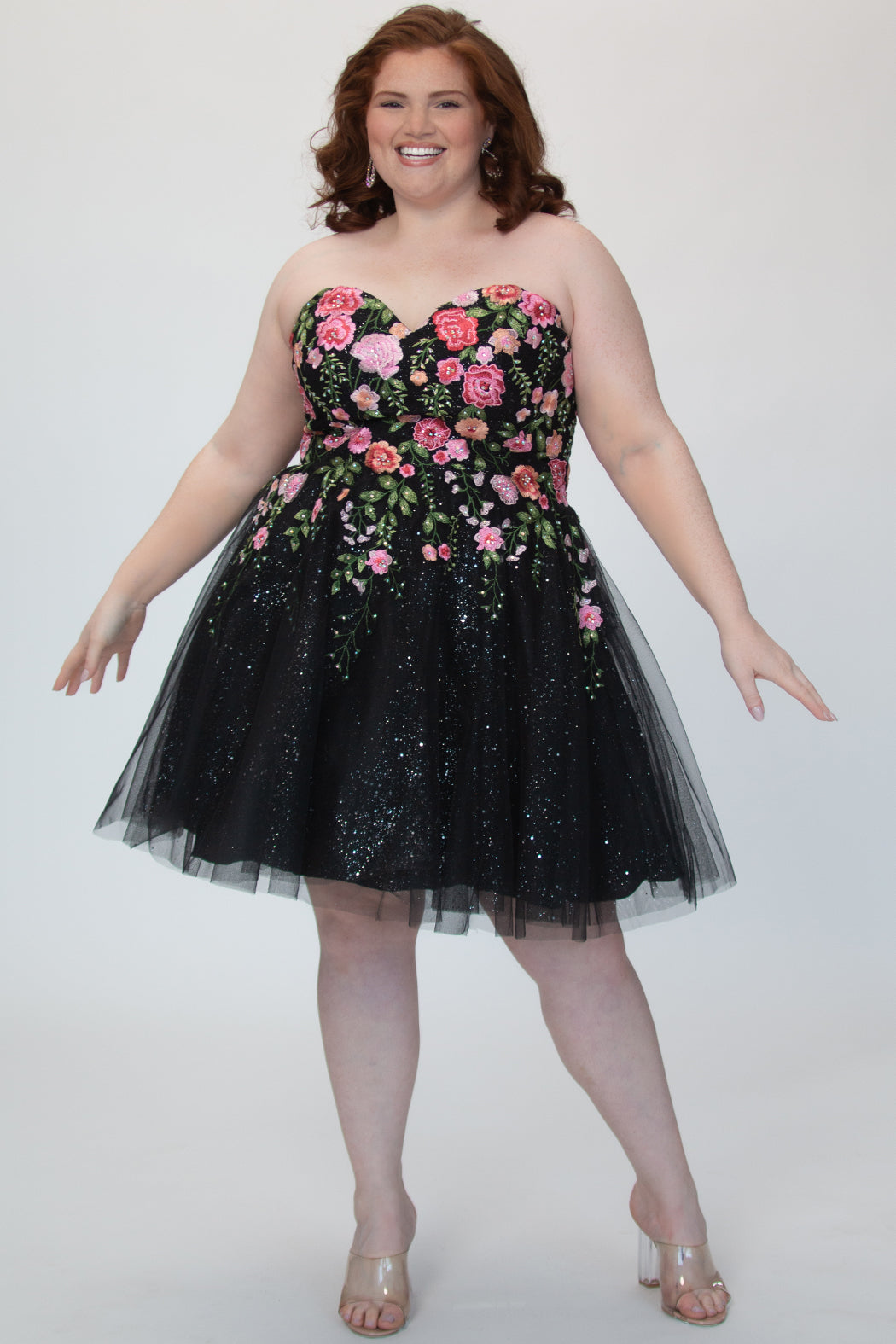 SC8137 Front view. Black sparkle tulle short a-line party dress with pink floral embroidered roses. Strapless sweetheart neckline, long invisible center back zipper.  Available only in black floral. Curvy sizes 10-32. Model in picture is 5 foot 9 inches and a size 16.