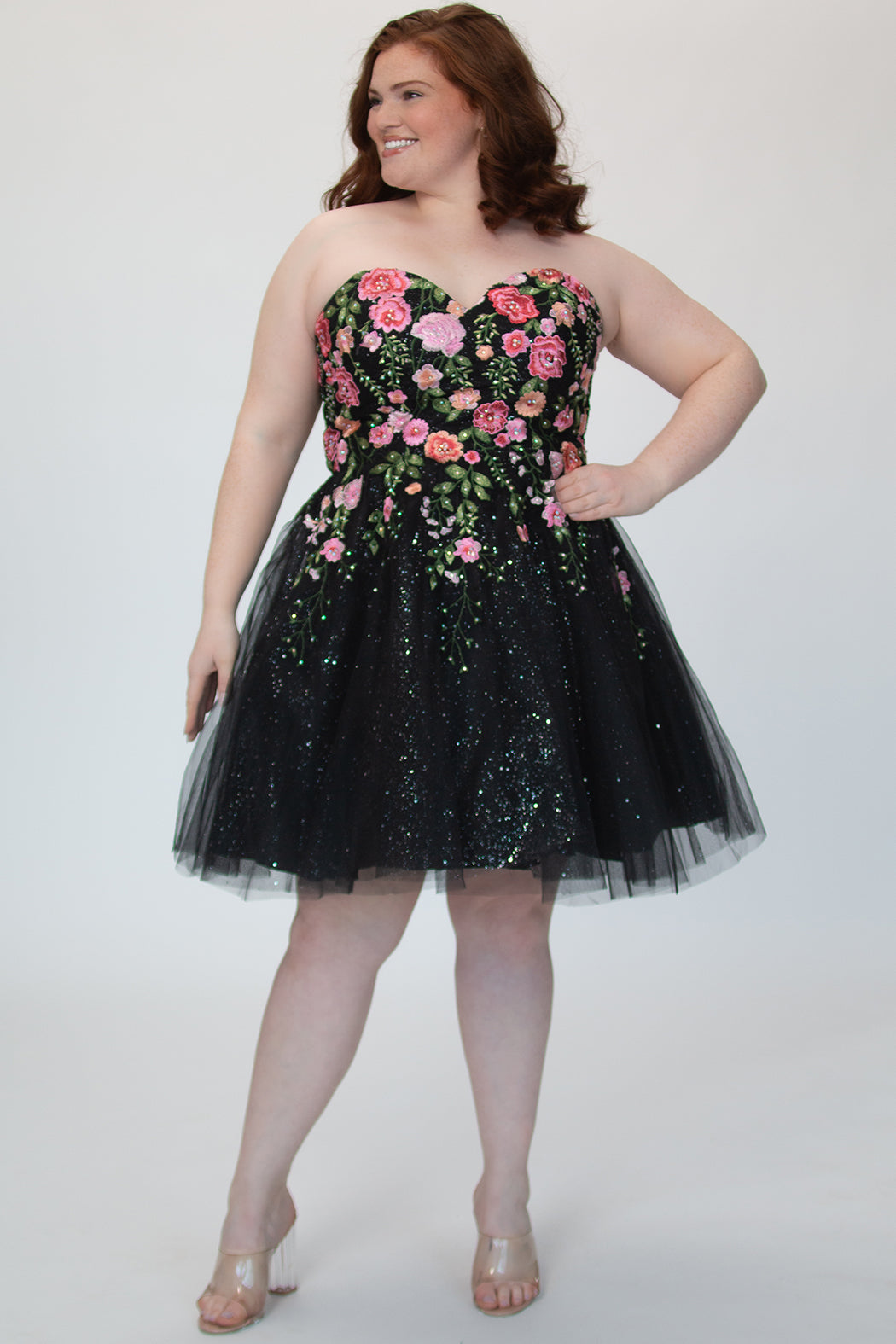 SC8137 Front view. Black sparkle tulle short a-line party dress with pink floral embroidered roses. Strapless sweetheart neckline, long invisible center back zipper.  Available only in black floral. Curvy sizes 10-32. Model in picture is 5 foot 9 inches and a size 16.