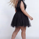 Short A-line plus size flowy party dress SC8153 by Sydney's Closet in the color Onyx black. Back view. Layers of dense sparkle tulle and a satin lining. V-neckline with thick bra-friendly straps and detachable bows at the top of the shoulder. Pleated bodice and 3 inch pleated waistband. Pockets and long invisible center back zipper. Available in Shamrock green, Admiral blue, Firecracker red and Shamrock green in sizes 14-32. Model is 5'9. 