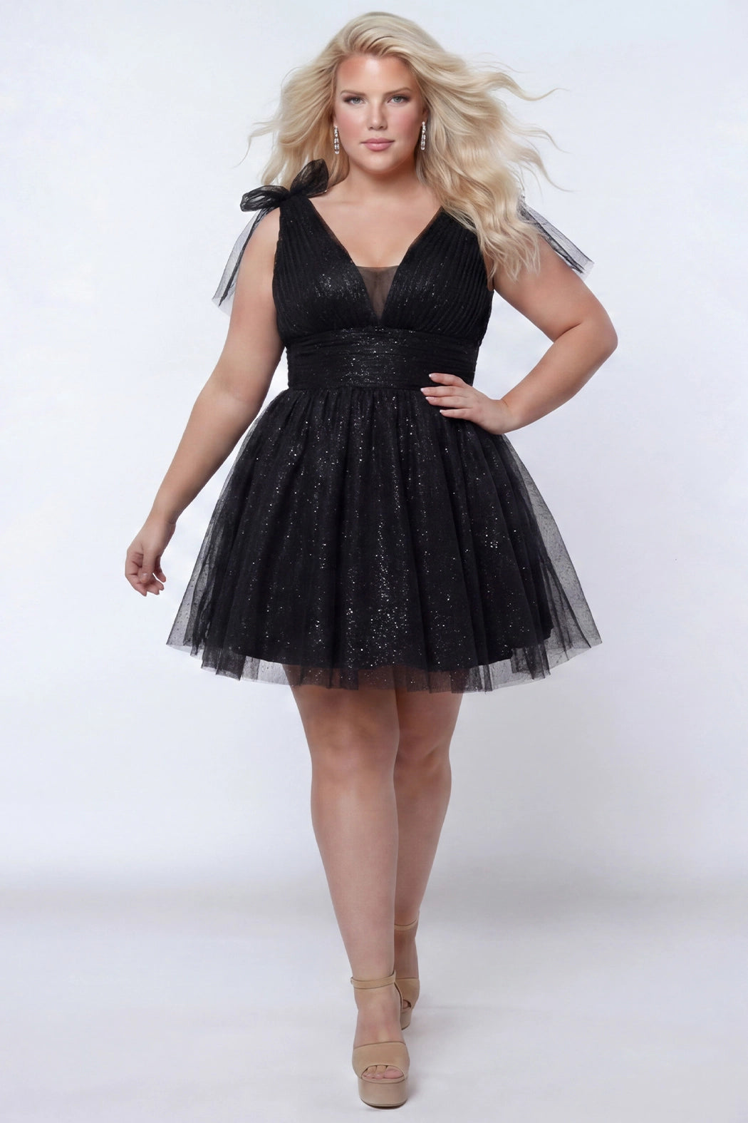 Short A-line plus size flowy party dress SC8153 by Sydney's Closet in the color Onyx black. Front view. Layers of dense sparkle tulle and a satin lining. V-neckline with thick bra-friendly straps and detachable bows at the top of the shoulder. Pleated bodice and 3 inch pleated waistband. Pockets and long invisible center back zipper. Available in Shamrock green, Admiral blue, Firecracker red and Shamrock green in sizes 14-32. Model is 5'9. 
