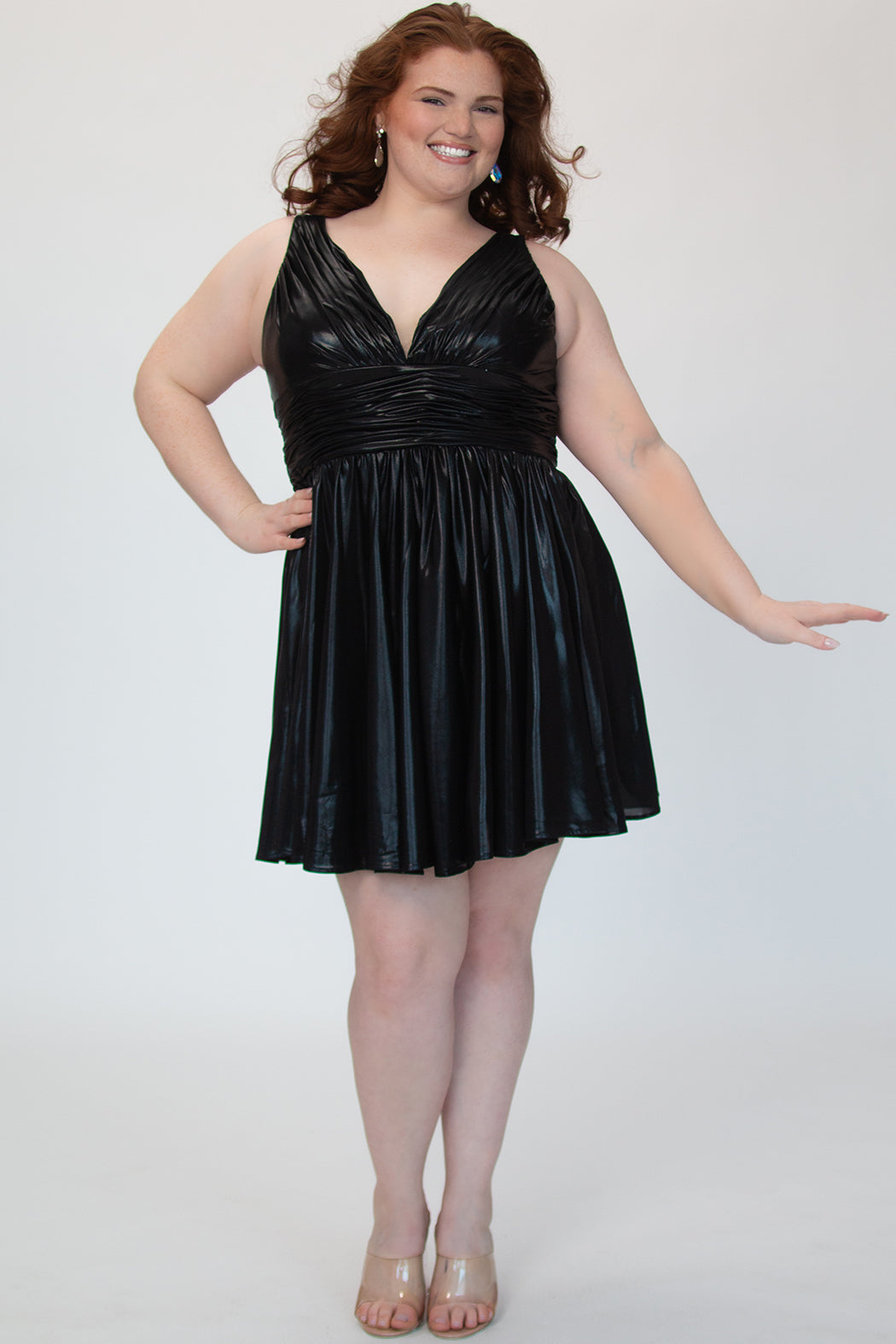 A-line flowy short party dress, SC8156 by Sydney's Closet. Front view. In the color raven black, a  metallic knit fabric. Thick bra-friendly straps, pleated v-neckline bodice and waist band, long invisible center back zipper. V- back. Available in Prism, Peacock and Raven black, sizes 14-32. 
Model in picture is 5'9. 