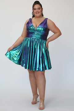 A-line flowy short party dress, SC8156 by Sydney's Closet. Front view. In the color Peacock, a  blue/green metallic knit fabric. Thick bra-friendly straps, pleated v-neckline bodice and waist band, long invisible center back zipper. V- back. Available in Prism, Peacock and Raven black, sizes 14-32. 
Model in picture is 5'9. 