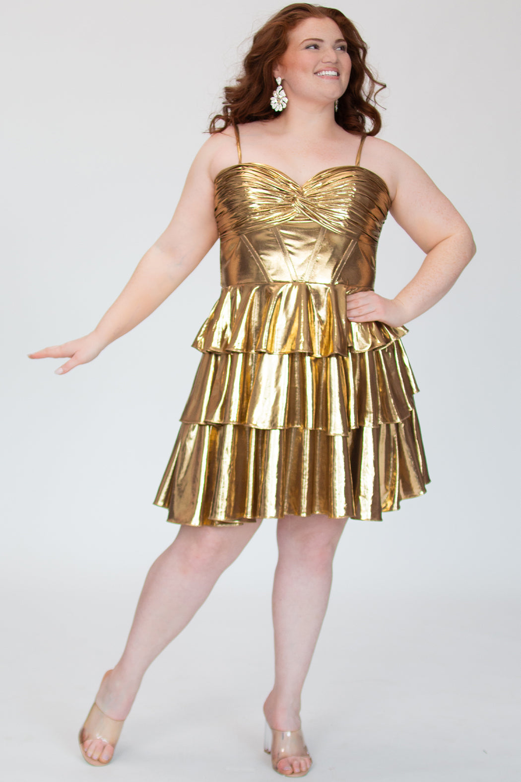 SC8161, metallic gold flowy plus size party dress by Sydney's Closet. Front view. Ruched knotted bodice with spaghetti straps, exposed boning and lace up back with modesty panel. A-line tiered skirt. Metallic stretch knit and knit lining. Available in Ruby red and Gold, sizes 14-24. 