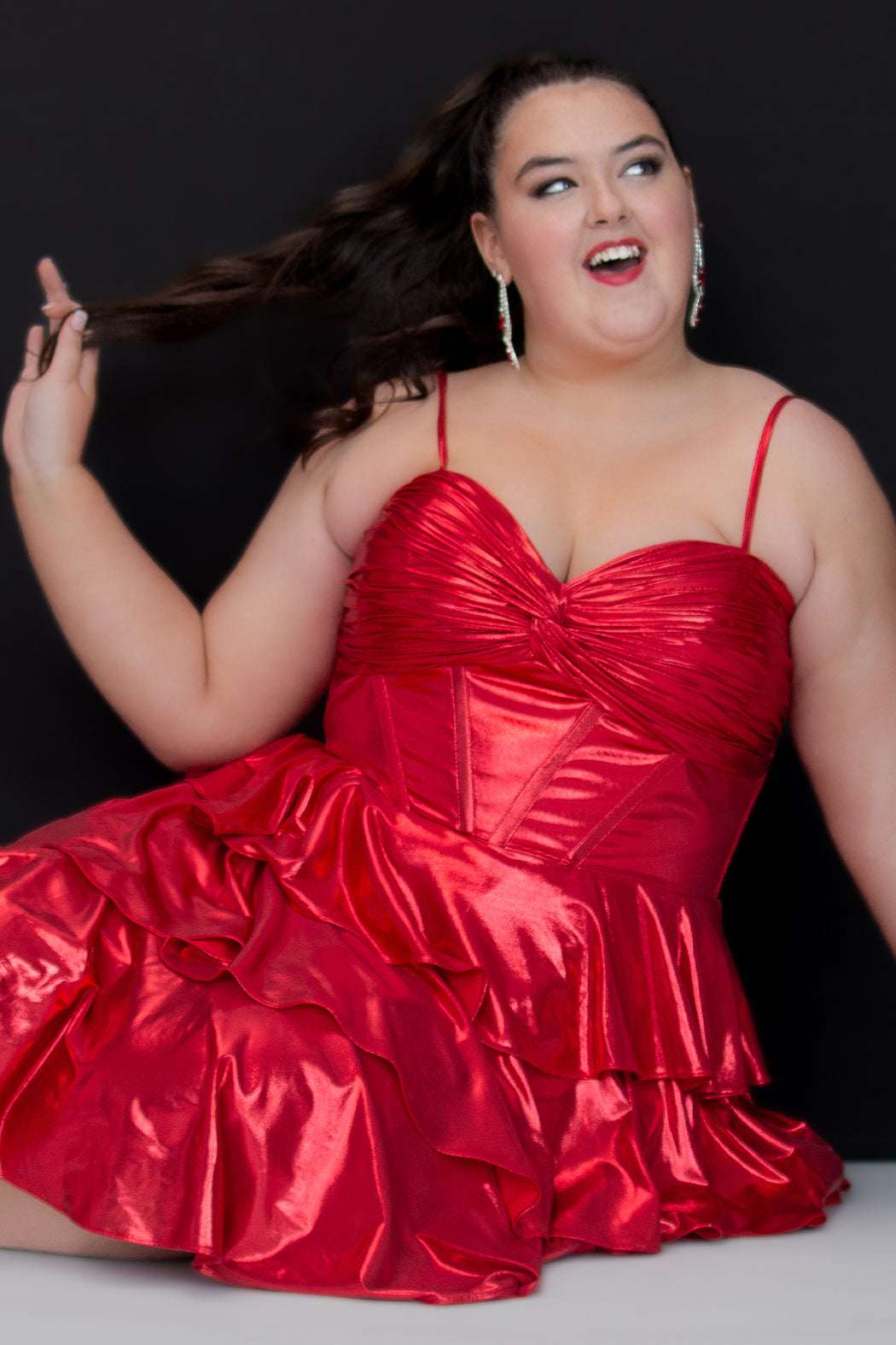 SC8161, Ruby Red flowy plus size party dress by Sydney's Closet. Ruched knotted bodice with spaghetti straps, exposed boning and center back zipper. A-line tiered skirt. Metallic stretch knit and knit lining. Available in Ruby red and Gold, sizes 14-24. 
