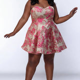 Plus-size model wearing a strapless, leeveless A-line mini dress with a sweetheart neckline and metallic floral brocade pattern in pink, gold, and champagne tones. The dress features a fitted bodice and a flared skirt with soft pleats. She is styled with long wavy black hair, statement earrings, and nude platform ankle-strap heels, posing against a light gray studio background.

Sydney's Closet SC8165 in Pink Floral