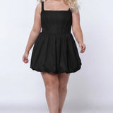 Plus-size model wearing a black sleeveless taffeta mini dress with a square neckline, structured corset-inspired bodice with exposed boning, and voluminous bubble hem skirt. She is styled with long flowing blonde hair, drop earrings, and nude platform ankle-strap heels, walking toward the camera against a light gray studio background. Front view.

Sydney's Closet SC8166 in black