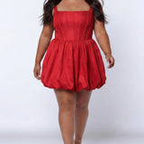Plus-size model wearing a red sleeveless taffeta mini dress with a square neckline, structured corset-inspired bodice with exposed boning, and voluminous bubble hem skirt. She is styled with long flowing brown hair, drop earrings, and nude platform ankle-strap heels, walking toward the camera against a light gray studio background. Front view.

Sydney's Closet SC8166 in red