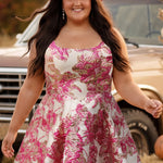 Plus-size model wearing a sleeveless a-line mini dress with a scoop neckline and metallic floral brocade pattern in shades of pink, fuchsia, and champagne. She is styled with a pink glitter cowboy hat, long flowing dark brown hair, dangling earrings, and nude ankle-strap heels. The model walks through a rustic autumn setting with pumpkins, hay bales, and a vintage tan truck in the background.

Sydney's Closet SC8169 in pink floral