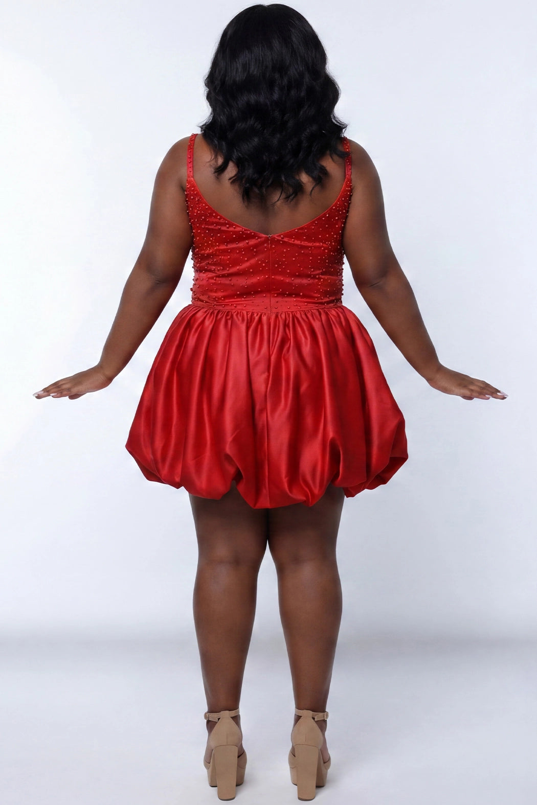 Plus-size model wearing a red sleeveless mini dress with a scoop back, rhinestone & pearl embellished fitted bodice, and a voluminous bubble hem skirt and center back zipper. She is styled with long wavy black hair, dangling crystal earrings, and nude platform ankle-strap heels, posing against a light gray studio background while.

Sydney's Closet SC8171 in red