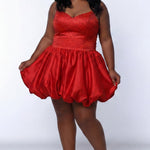 Plus-size model wearing a red sleeveless mini dress with a V-neckline, rhinestone & pearl embellished fitted bodice, and a voluminous bubble hem skirt. She is styled with long wavy black hair, dangling crystal earrings, and nude platform ankle-strap heels, posing against a light gray studio background while holding the sides of the skirt.

Sydney's Closet SC8171 in red
