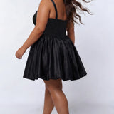 Plus-size model wearing a black sleeveless mini dress with a structured corset-style bodice and sweetheart neckline. The dress features lace detailing on the bodice and a voluminous satin bubble hem skirt. She is styled with long wavy dark brown hair, dangling earrings, and clear open-toe heels, posing against a light gray studio background while walking away. Back view. 

Sydney's Closet SC8173