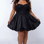 Plus-size model wearing a black sleeveless mini dress with a structured corset-style bodice and sweetheart neckline. The dress features lace detailing on the bodice and a voluminous satin bubble hem skirt. She is styled with long wavy dark brown hair, dangling earrings, and clear open-toe heels, posing against a light gray studio background while holding the sides of the skirt. Front view. 

Sydney's Closet SC8173