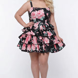 Plus-size model wearing a black and pink floral sleeveless mini dress with layered ruffle skirt. The dress features a square neckline, fitted bodice, and tiered ruffles at the waist and hem. She is styled with long wavy blonde hair, statement crystal earrings, and nude platform ankle-strap heels, posing against a studio background. Front view. 

Sydney's Closet SC8174