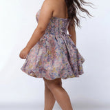 Plus-size model wearing a strapless a-line mini dress in purple floral brocade with metallic gold accents. The dress features a structured corset-style bodice with a strapless sweetheart neckline and a voluminous bubble hem skirt. She is styled with long wavy dark brown hair, statement earrings, and nude platform ankle-strap heels, posing against a light gray studio background.

Sydney's Closet SC8177 in purple floral