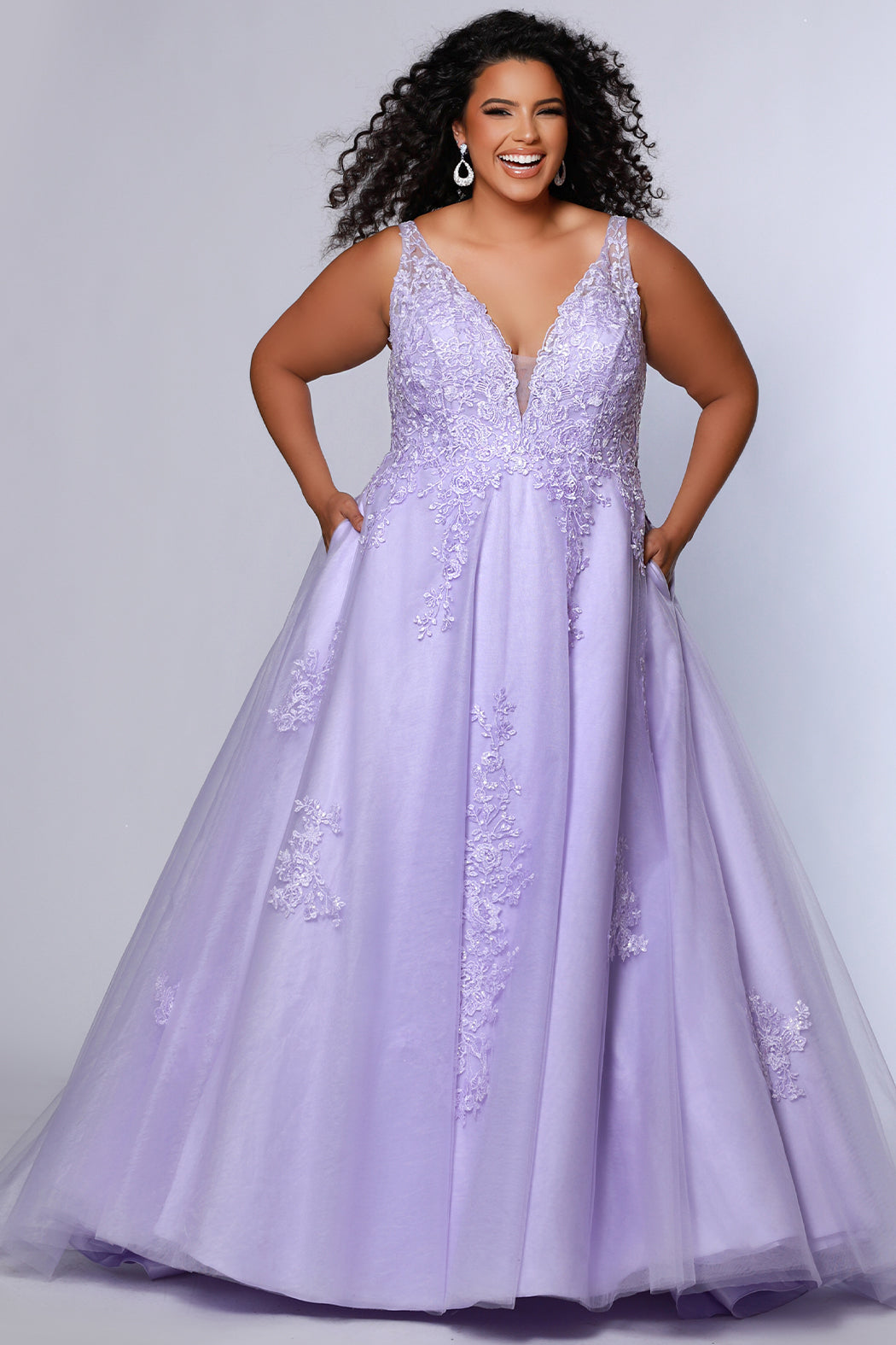 Plus size lace and tulle ball gown by Tease Prom.  Style TE2526 available in lilac purple or sage green.  Deep v-neckline with nude mesh insert. Wide straps and bodice fully covered with appliques.  Bodice is unlined but ships with optional lining panel.  Full A-line skirt with scattered lace appliques, pockets and chapel train. 