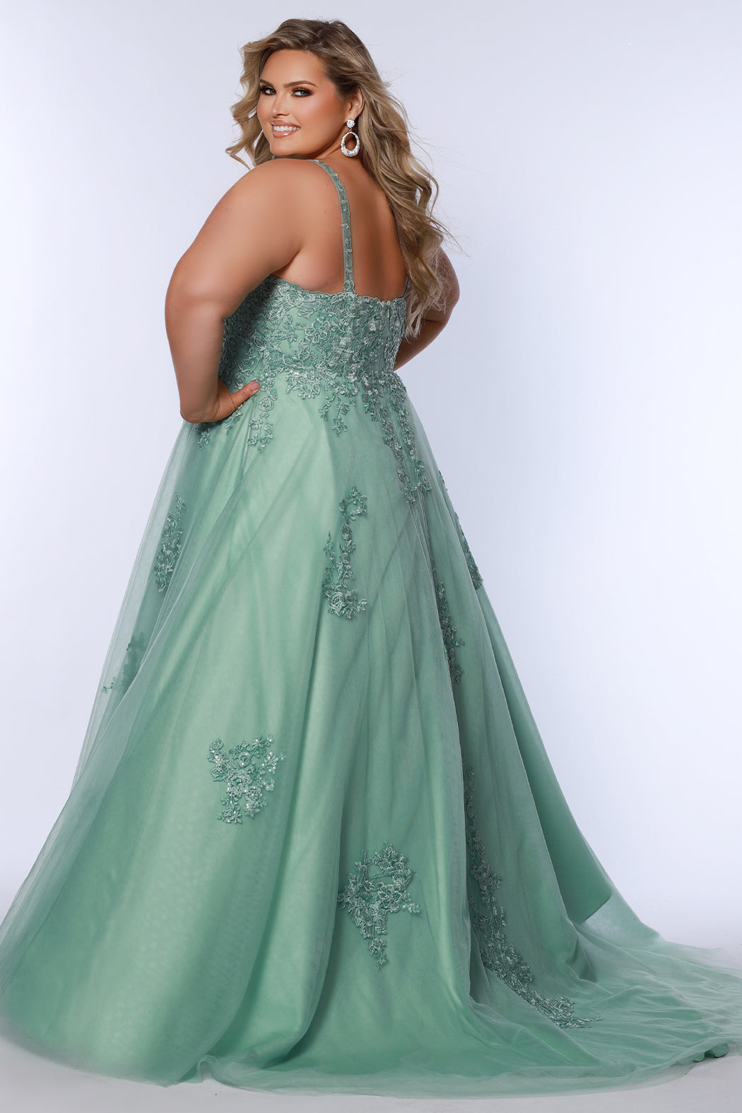 Plus size lace and tulle ball gown by Tease Prom.  Style TE2526 available in lilac purple or sage green.  Deep v-neckline with nude mesh insert. Wide straps and bodice fully covered with appliques.  Bodice is unlined but ships with optional lining panel.  Full A-line skirt with scattered lace appliques, pockets and chapel train. 