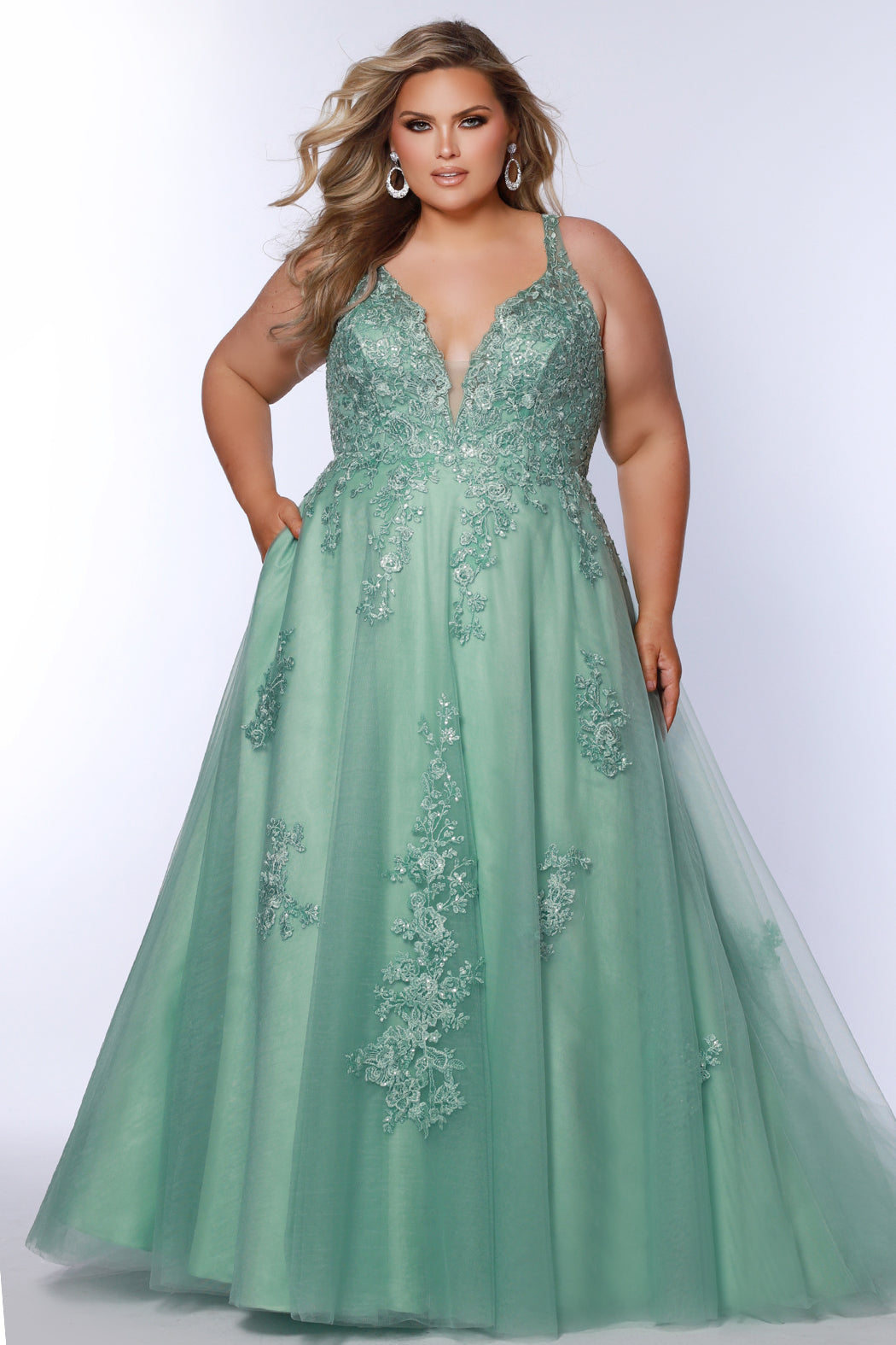 Plus size lace and tulle ball gown by Tease Prom.  Style TE2526 available in lilac purple or sage green.  Deep v-neckline with nude mesh insert. Wide straps and bodice fully covered with appliques.  Bodice is unlined but ships with optional lining panel.  Full A-line skirt with scattered lace appliques, pockets and chapel train. 