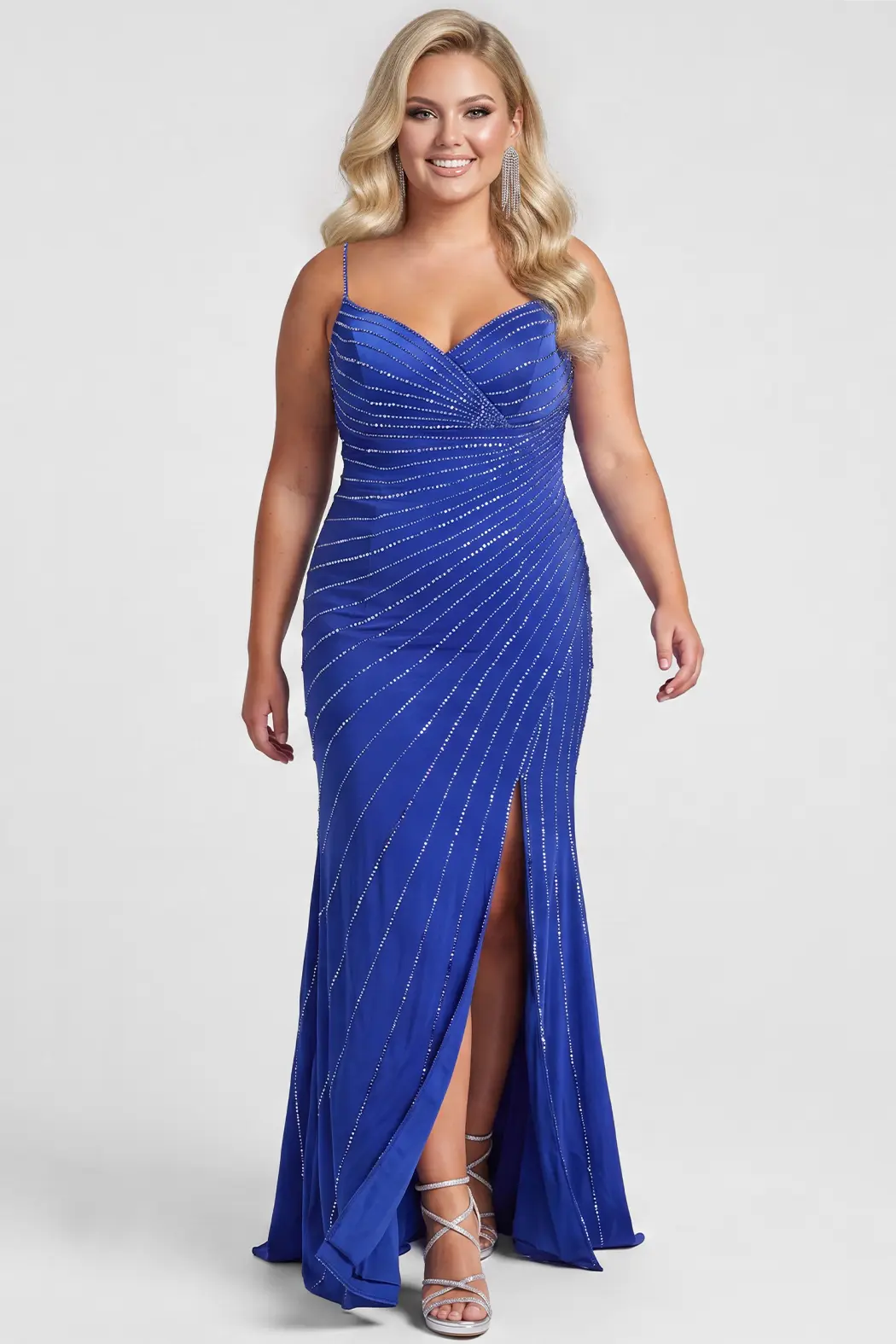 A blonde teen modeling a royal blue floor-length formal gown with thin straps, a sweetheart neckline, diagonal silver hot fix stone embellishments, and a high front slit, photographed against a light gray studio background.

TE2705 in royal by Tease Prom, exclusively plus size prom dresses designed by Sydney's