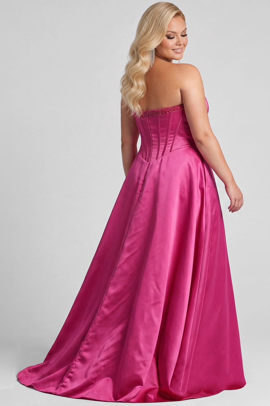 A blonde model wears a bright fuchsia pink strapless satin gown with a structured corset-style bodice, beaded upper bodice and a full skirt with a thigh-high slit, photographed against a light gray studio background.

TE2708 in fuchsia pink by Tease Prom, exclusively plus size prom dresses designed by Sydney's Closet
