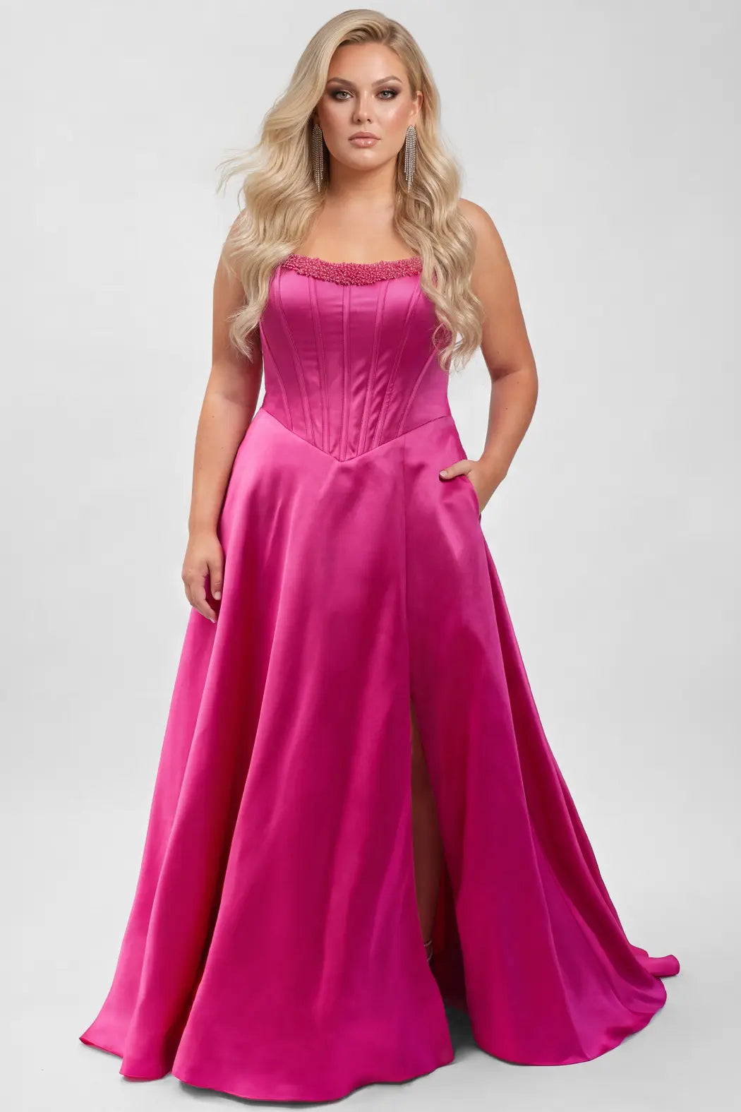A blonde model wears a bright fuchsia pink strapless satin gown with a structured corset-style bodice, beaded upper bodice and a full skirt with a thigh-high slit, photographed against a light gray studio background.

TE2708 in fuchsia pink by Tease Prom, exclusively plus size prom dresses designed by Sydney's Closet