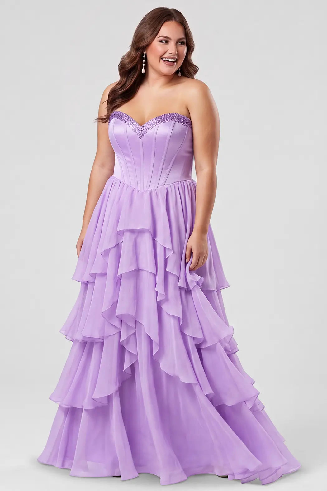 A brunette teen modeling a strapless lilac purple formal gown with a beaded sweetheart neckline, exposed corset boning, basque waistline and a full tiered ruffle skirt, photographed against a light gray studio background.

TE2709 in lilac by Tease Prom, exclusively plus size prom dresses designed by Sydney's Closet.