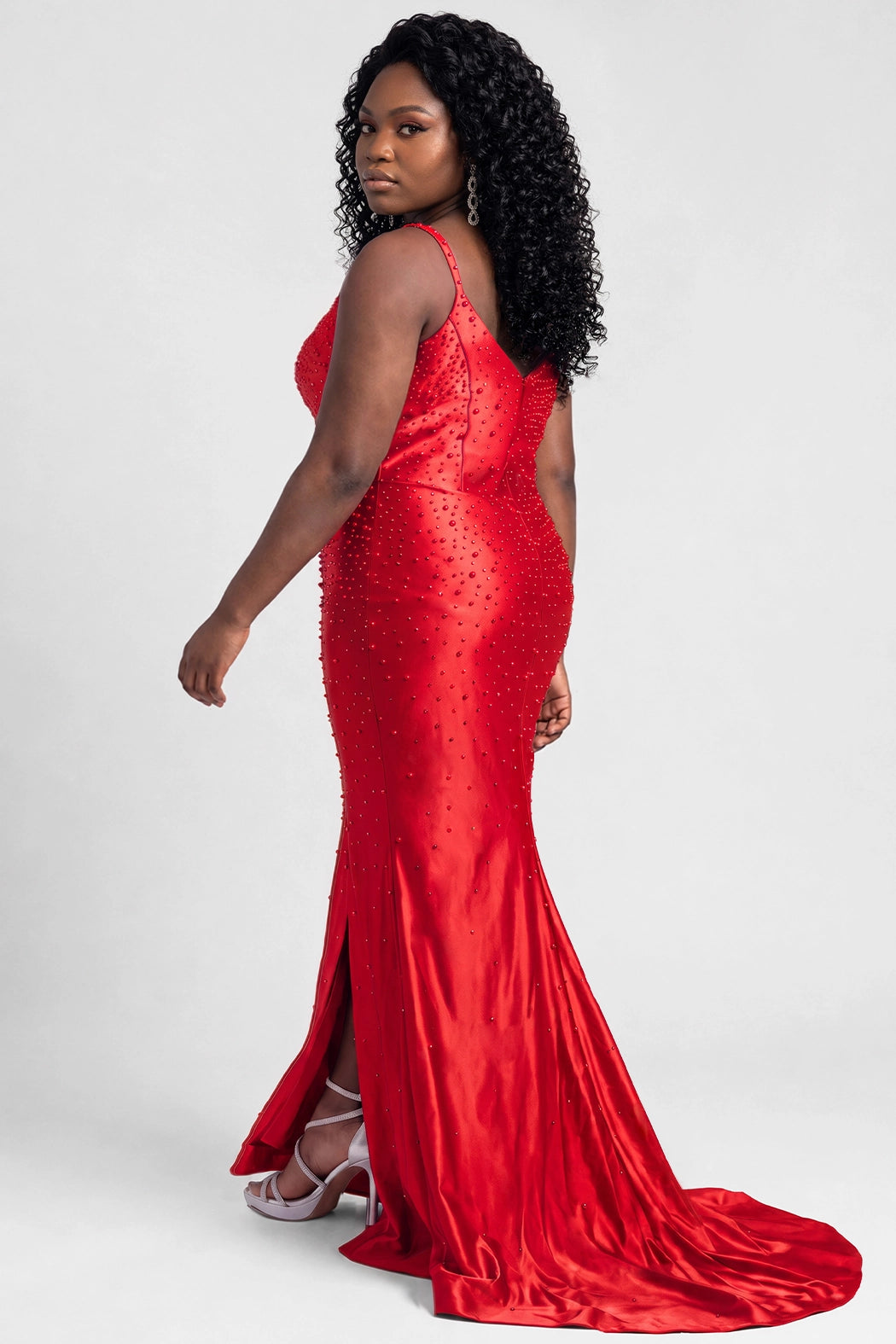 A teenager modeling a floor-length red slim fitted evening gown with a plunging V-neckline, pearl and beaded embellishments, and a thigh-high front slit, photographed against a light gray studio background.

TE2712 in ruby red by Tease Prom, exclusively plus size prom dresses designed by Sydney's Closet.