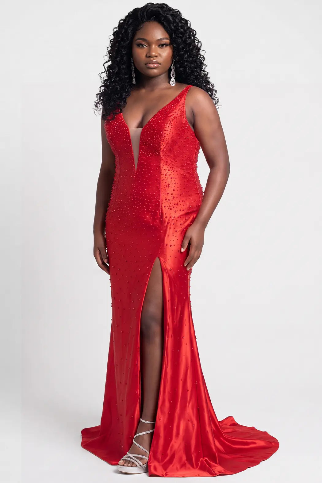 A teenager modeling a floor-length red slim fitted evening gown with a plunging V-neckline, pearl and beaded embellishments, and a thigh-high front slit, photographed against a light gray studio background.

TE2712 in ruby red by Tease Prom, exclusively plus size prom dresses designed by Sydney's Closet.