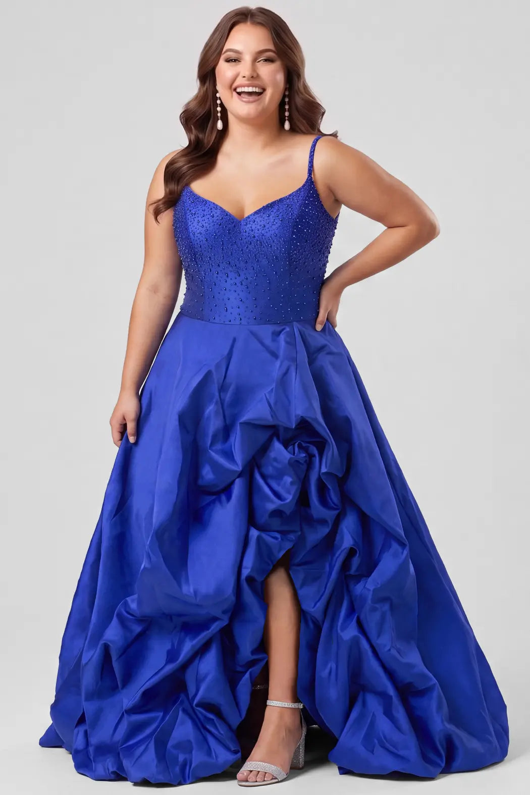 A teenager modeling a royal blue ball gown with a pearl and beaded sweetheart bodice, spaghetti straps, drop waistline and a high-low ruffled hemline, photographed against a light gray studio background.

TE2713 in cobalt blue by Tease Prom, exclusively plus size prom dresses designed by Sydney's Closet.
