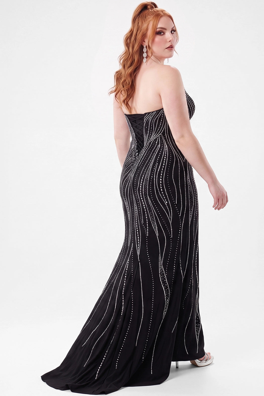 A teenager modeling a strapless black slim fitted evening gown with silver beaded vertical lines and a slight train, photographed against a plain light gray studio background.

TE2714 in moonstone black by Tease Prom, exclusively plus size prom dresses designed by Sydney's Closet.