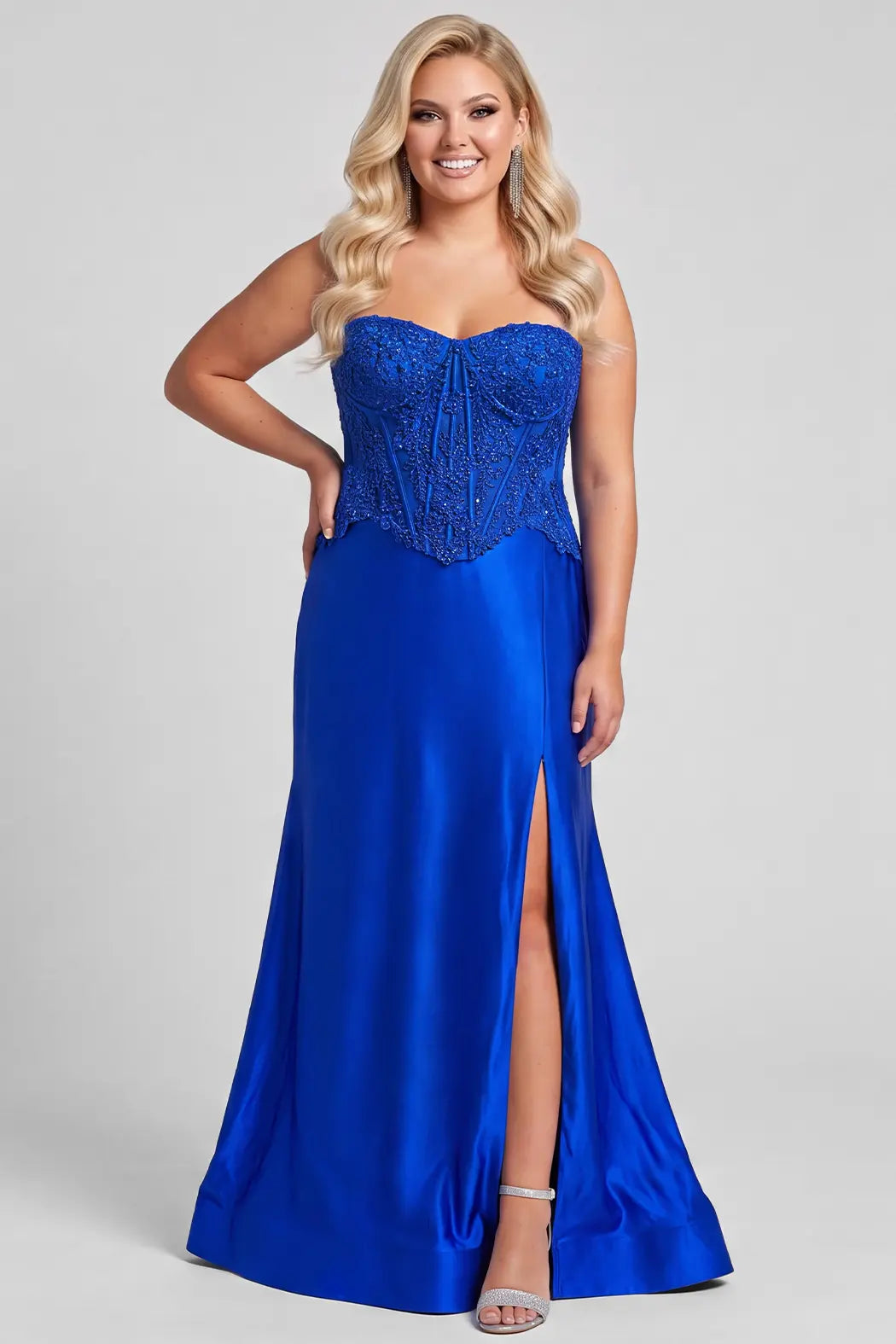 A blonde model wearing a strapless royal blue fitted evening gown with a lace and hot fix corset-style bodice and a high front slit, photographed against a light gray studio background.

TE2718 in royal by Tease Prom, exclusively plus size prom dresses designed by Sydney's Closet.