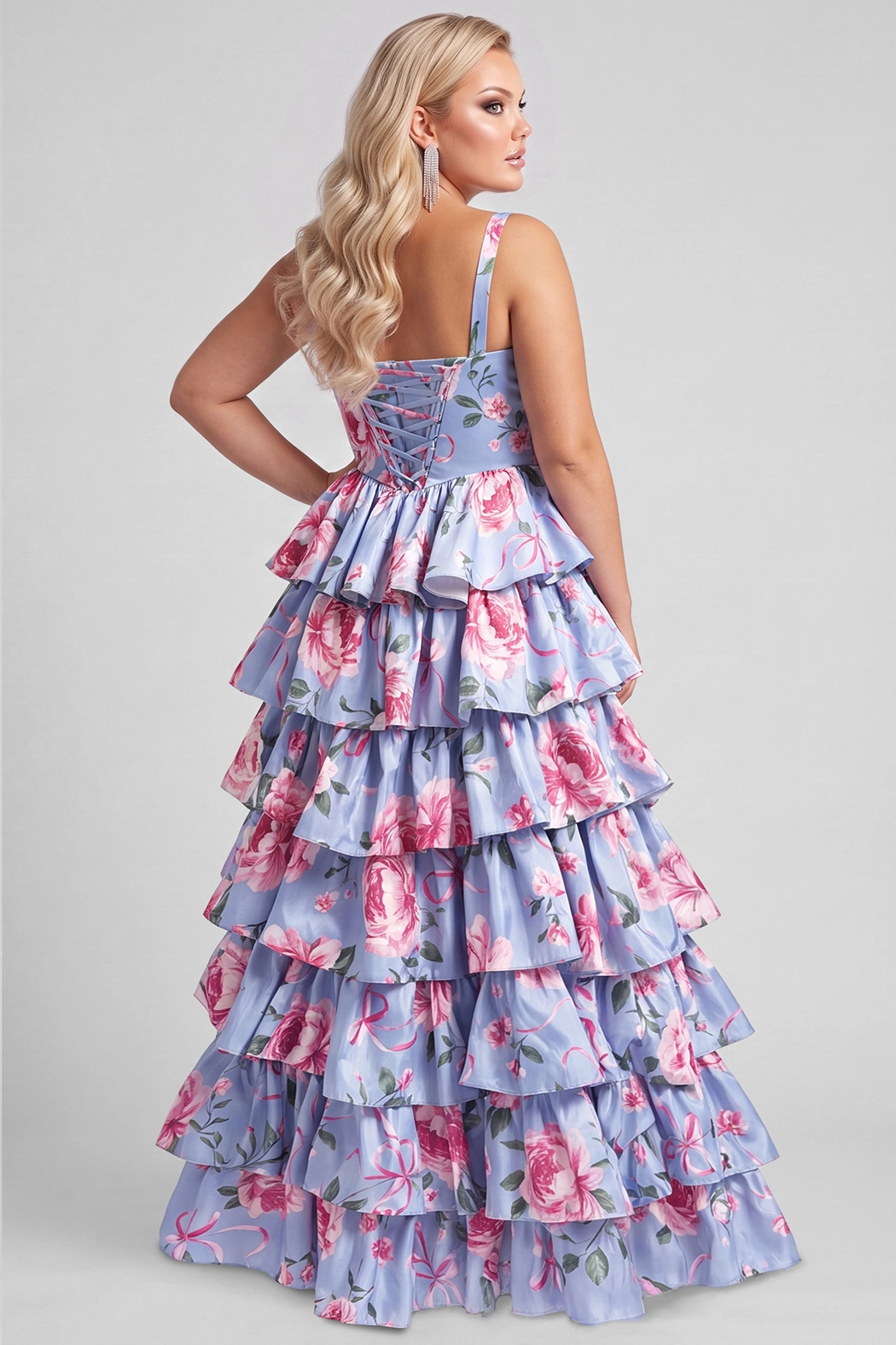 A blond teenager modeling a strapless tiered formal dress with a lavender-blue background and a pink floral print, set against a solid gray studio backdrop. The dress featured a basque waisltine and tiered A-line skirt.

TE2719 in blue floral by Tease Prom, exclusively plus size prom dresses designed by Sydney's Closet.