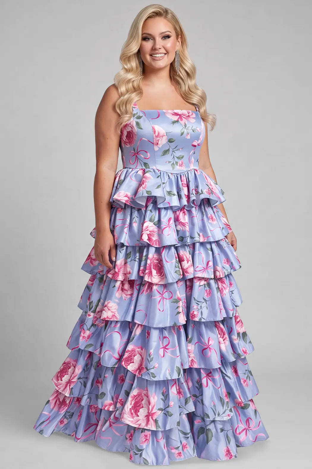 A blond teenager modeling a strapless tiered formal dress with a lavender-blue background and a pink floral print, set against a solid gray studio backdrop. The dress featured a basque waisltine and tiered A-line skirt.

TE2719 in blue floral by Tease Prom, exclusively plus size prom dresses designed by Sydney's Closet.